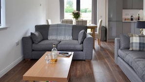 Ein modernes Wohnzimmer mit grauem Sofa, einem Holztisch und einem Essbereich mit Tisch und Stühlen.