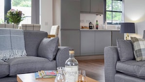 Ein modernes Wohnzimmer mit zwei grauen Sofas, einem Holztisch mit einer Flasche Coper Dog, einem Glas und einer Zeitschrift.