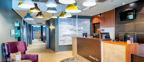A hotel reception area with a wooden reception desk, multiple pendant lights, a wall with motivational words, and a check-in counter.