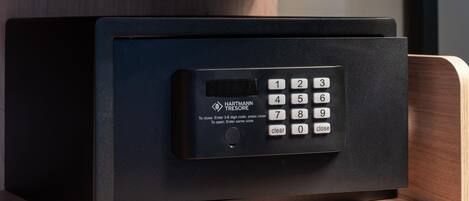 A black safe with a digital keypad, labeled 'HARTMANN TREASURE,' on a wooden shelf.