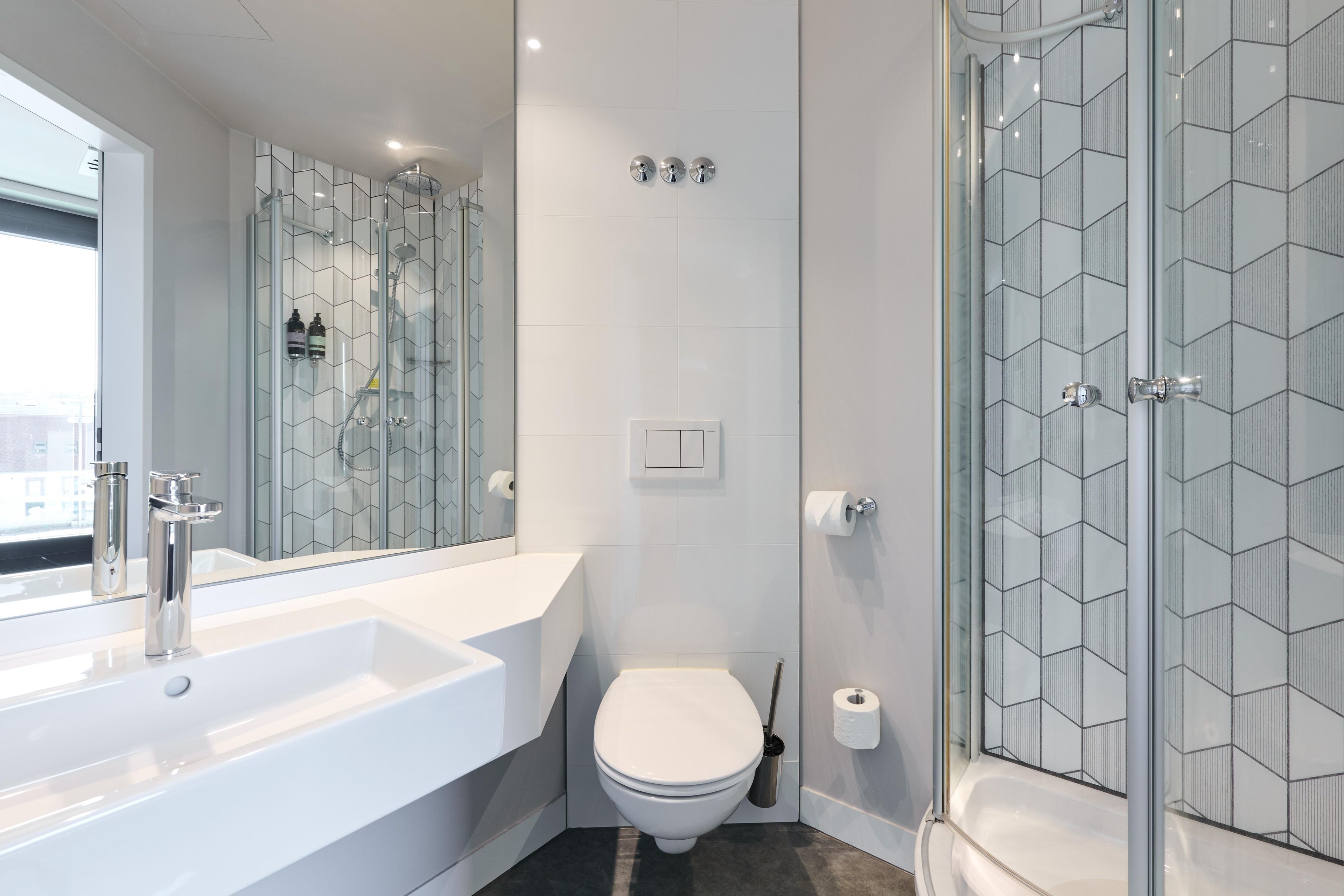 A modern bathroom with a large white sink, a toilet, and a glass-enclosed shower area.