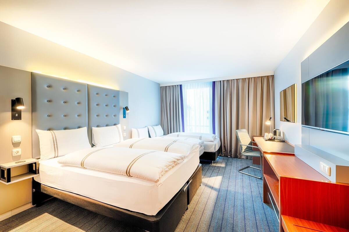 A hotel room with a large bed, a desk, a TV, and a headboard with a light panel.