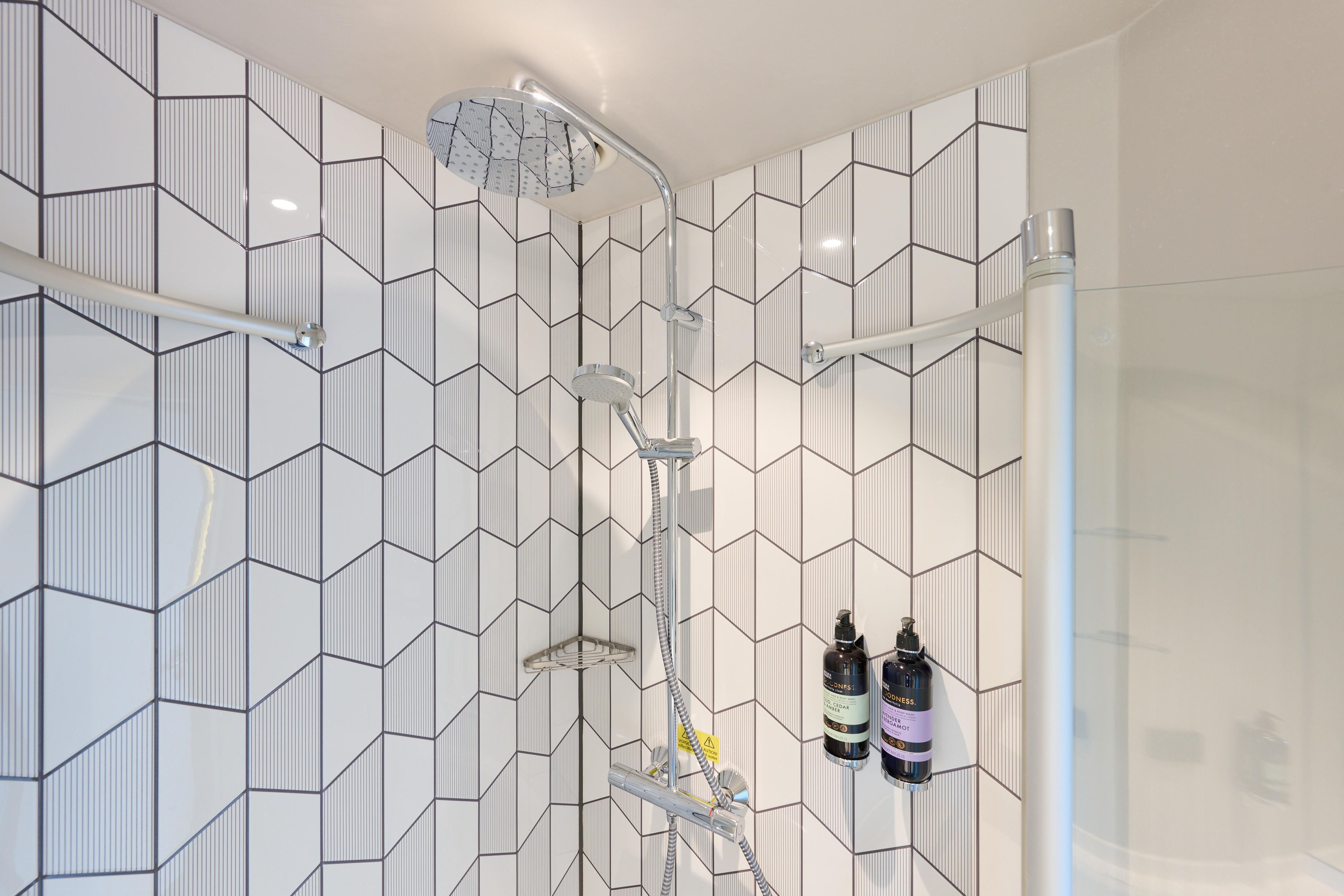 A modern bathroom with a geometric tile pattern, a shower with a rain showerhead, and two bottles of hair product on the wall.