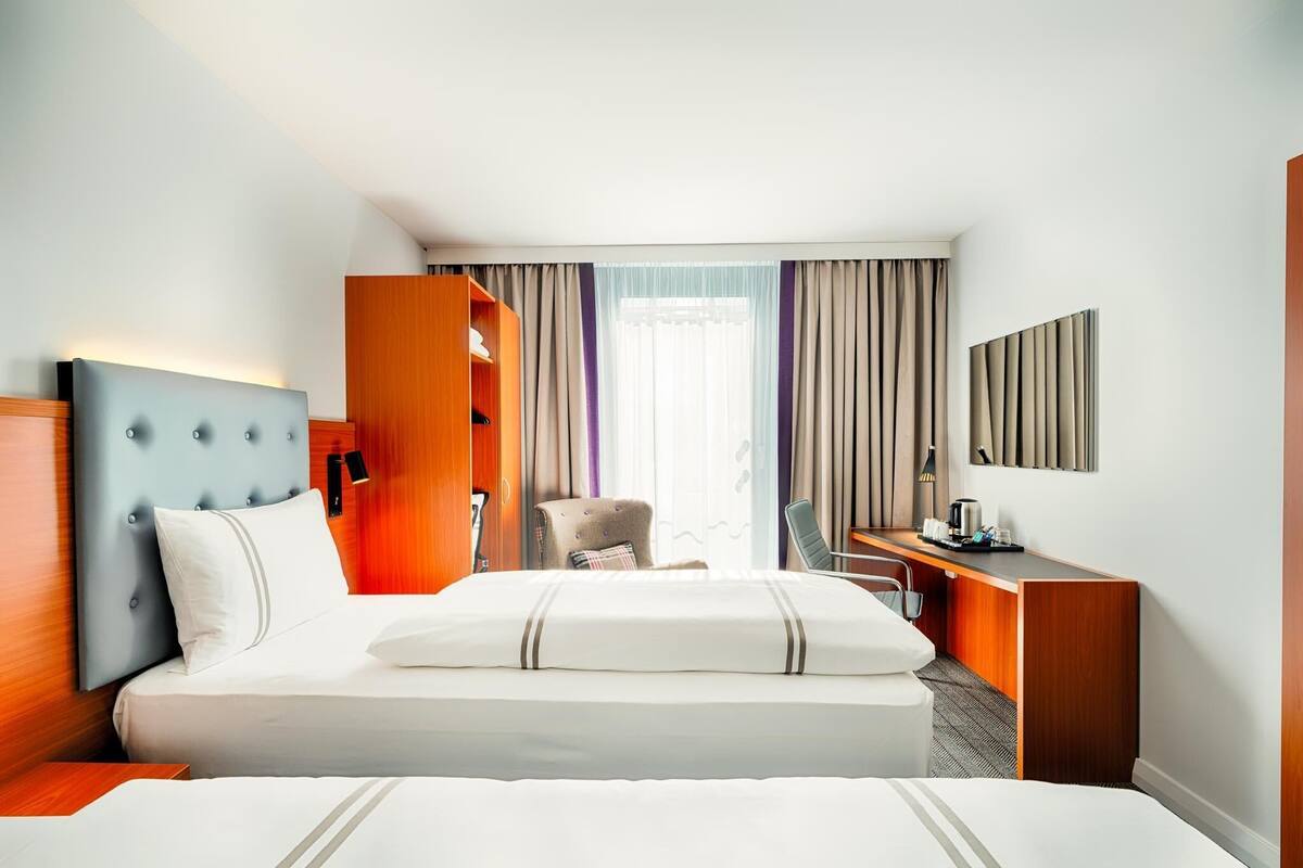 A hotel room with a bed, a desk, a chair, a wardrobe, and a large window with curtains.