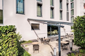 A building with a covered outdoor seating area, multiple windows, and a staircase leading to an entrance. - Premier Inn Frankfurt City Europaviertel (Frankfurt)