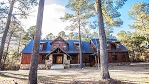 A rustic cabin with a stone foundation, a wooden exterior, and a blue metal roof, surrounded by tall trees.