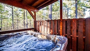 A hot tub with a wooden deck and a wooden fence, surrounded by trees.