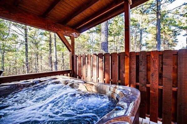 A hot tub with a wooden deck and a wooden fence, surrounded by trees.