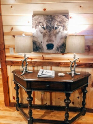 A wooden desk with two lamps, a notebook, and a framed picture of a wolf's face on the wall behind it.