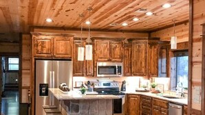 A spacious kitchen with wooden cabinets, a central island, stainless steel appliances, and pendant lighting.