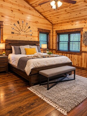 A wooden cabin bedroom with a bed, bench, and decorative wall art. - Stone Mountain Lodge – Spacious 6-Bedroom Forest Cabin (Broken Bow)