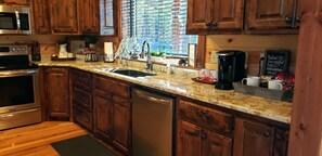 A kitchen with wooden cabinets, a granite countertop, stainless steel appliances, and a window with blinds.