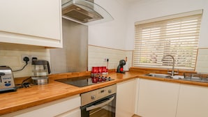 A modern kitchen with a built-in oven, a coffee maker, and a kettle on the countertop. - Oak Tree Cottage (Cardigan)