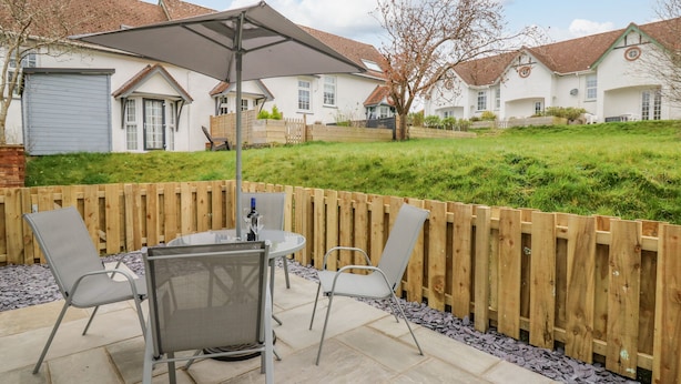 A patio with a table and chairs, a wooden fence, and houses in the background. - Oak Tree Cottage (Cardigan)