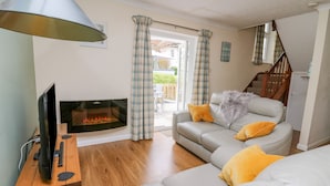 A living room with a fireplace, grey sofas, yellow cushions, a wooden TV stand, and a staircase. - Oak Tree Cottage (Cardigan)