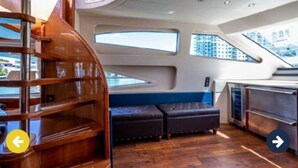 A yacht interior with a wooden staircase, a seating area with cushioned benches, and a kitchen area. - Luxury Italian Megayacht (Fajardo)