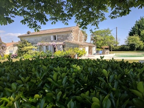 A stone house with a garden, a pool, and a red car parked outside.