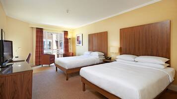 A hotel room with two beds, a desk, a chair, a TV, and a window with curtains.
