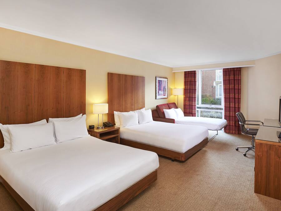 A hotel room with two beds, a desk, a chair, a television, and a window with curtains.