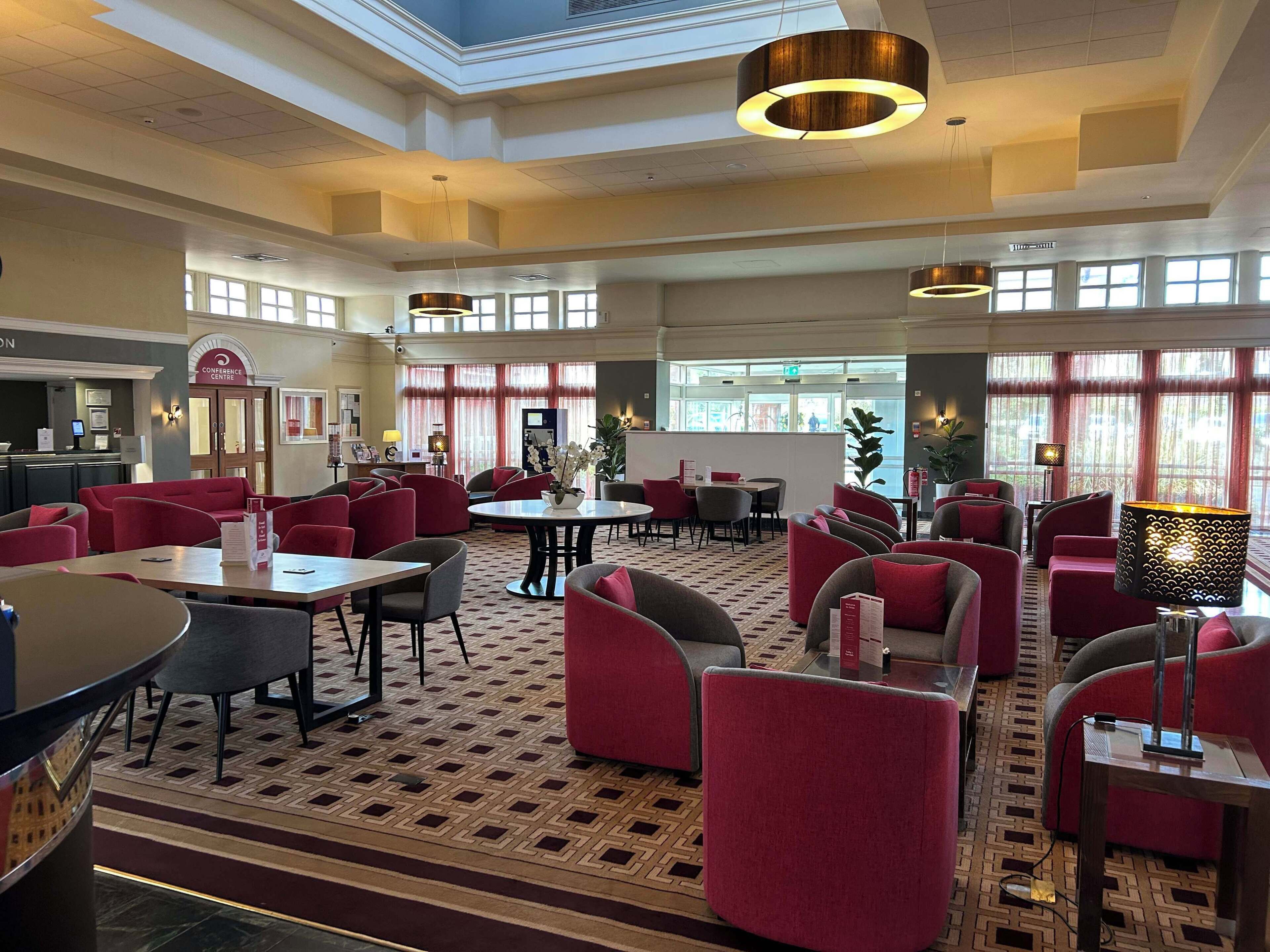 A spacious hotel lobby with multiple seating areas, a reception desk, and large windows allowing natural light.