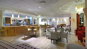 A hotel lobby with a bar area, seating arrangements, and a kitchen in the background.