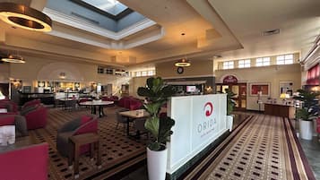 Vestíbulo de hotel con mostrador de recepción, zonas de estar, un reloj y una planta grande en maceta.