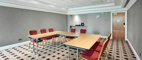 A conference room with a large table, red chairs, and patterned carpet.