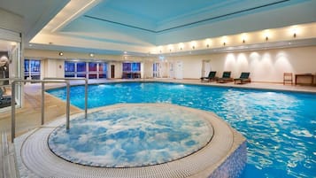 Una piscina interna con una vasca idromassaggio al centro, circondata da sedie a sdraio e un bar a bordo piscina.