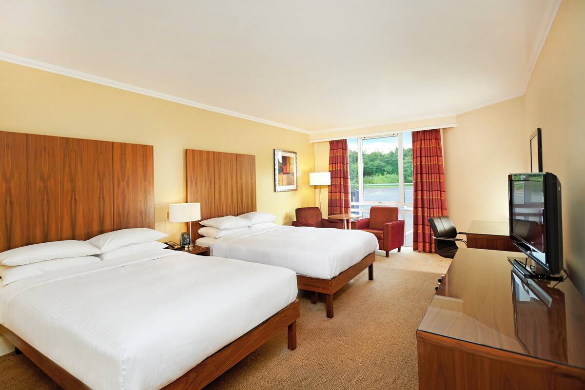 Ein Hotelzimmer mit zwei Betten, einem Schreibtisch, einem Stuhl, einem Fernseher und einem Fenster mit Vorhängen.