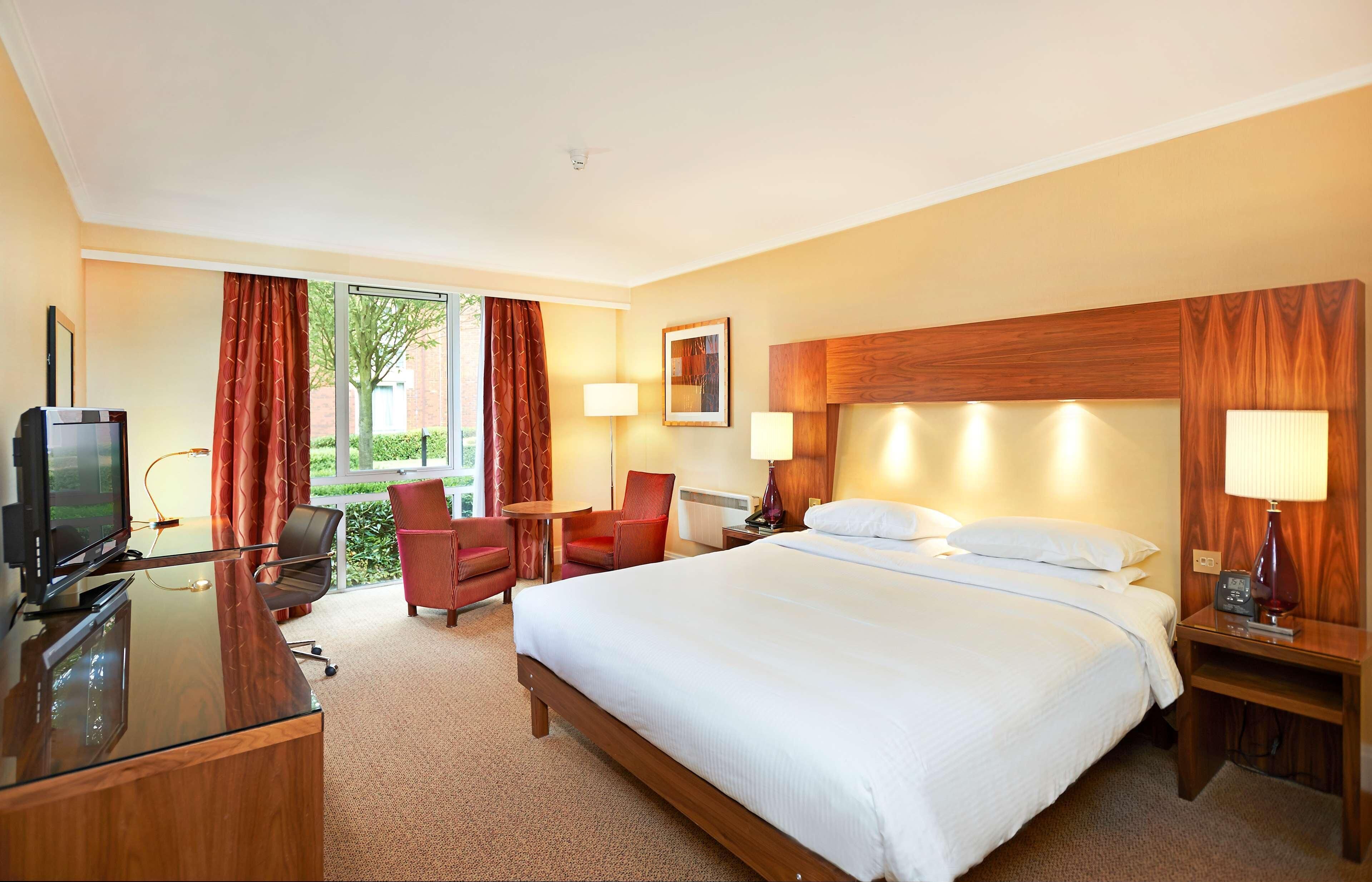 A hotel room with a bed, desk, TV, and seating area.