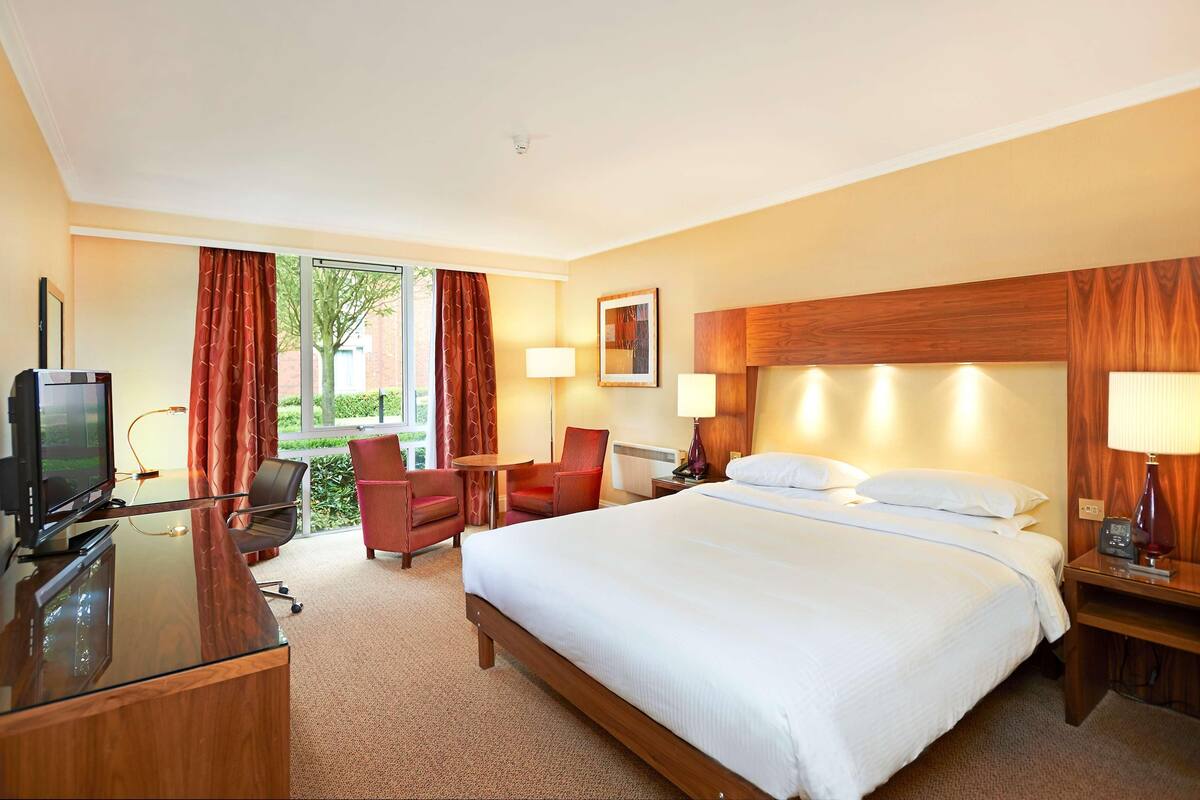 A hotel room with a bed, desk, TV, and seating area.