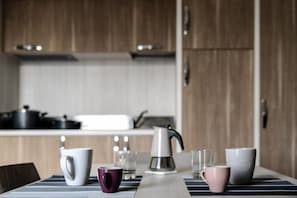A modern kitchen with wooden cabinets, a gas stove, and a coffee maker on a striped tablecloth.