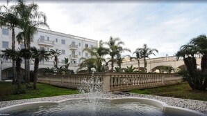 Un patio con una fuente, palmeras y un edificio con balcones.