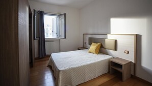 Un dormitorio con cama, mesita de noche, ventana con cortinas y radiador.