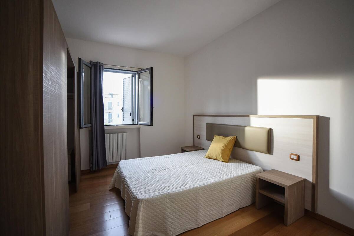 Een slaapkamer met een bed, nachtkastje, raam met gordijnen en een radiator.
