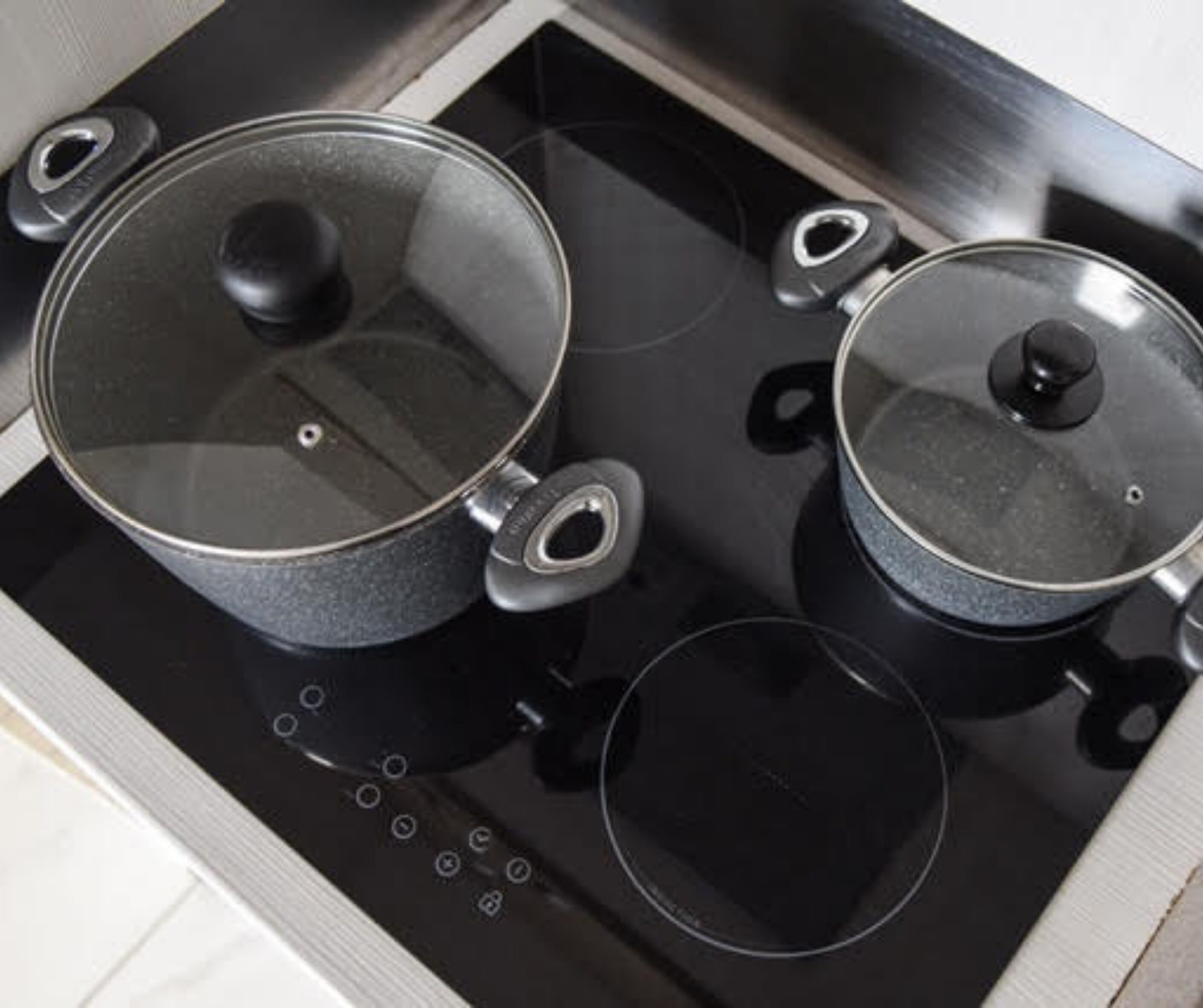 Una cocina con dos hornillas eléctricas, cada una con una olla con tapa de vidrio y una olla más pequeña.