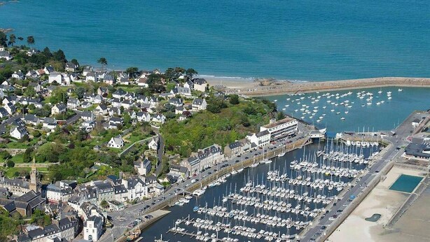 An aerial view of a coastal town with a marina filled with boats, residential buildings, and a prominent church tower. - Seaside house in large enclosed garden in Binic (Binic-Étables-sur-Mer)