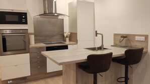 Una cocina compacta con microondas, horno y estufa moderna. Hay dos taburetes en una pequeña barra.