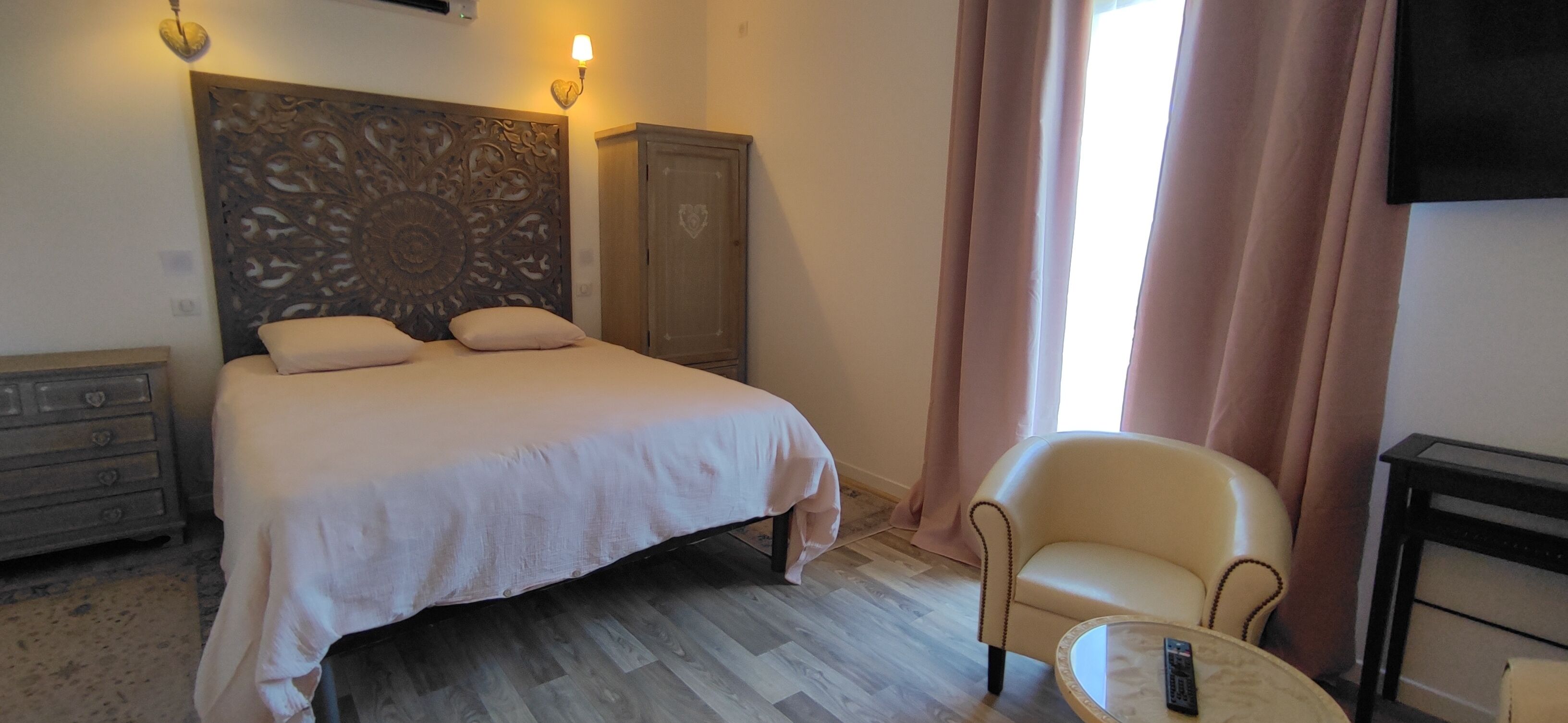 Une chambre d’hôtel avec un lit, une chaise, une petite table, une armoire et un téléviseur fixé au mur.
