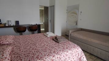Un dormitorio con cama, sofá, escritorio con sillas, cafetera y puerta decorada con un diseño de rosa.