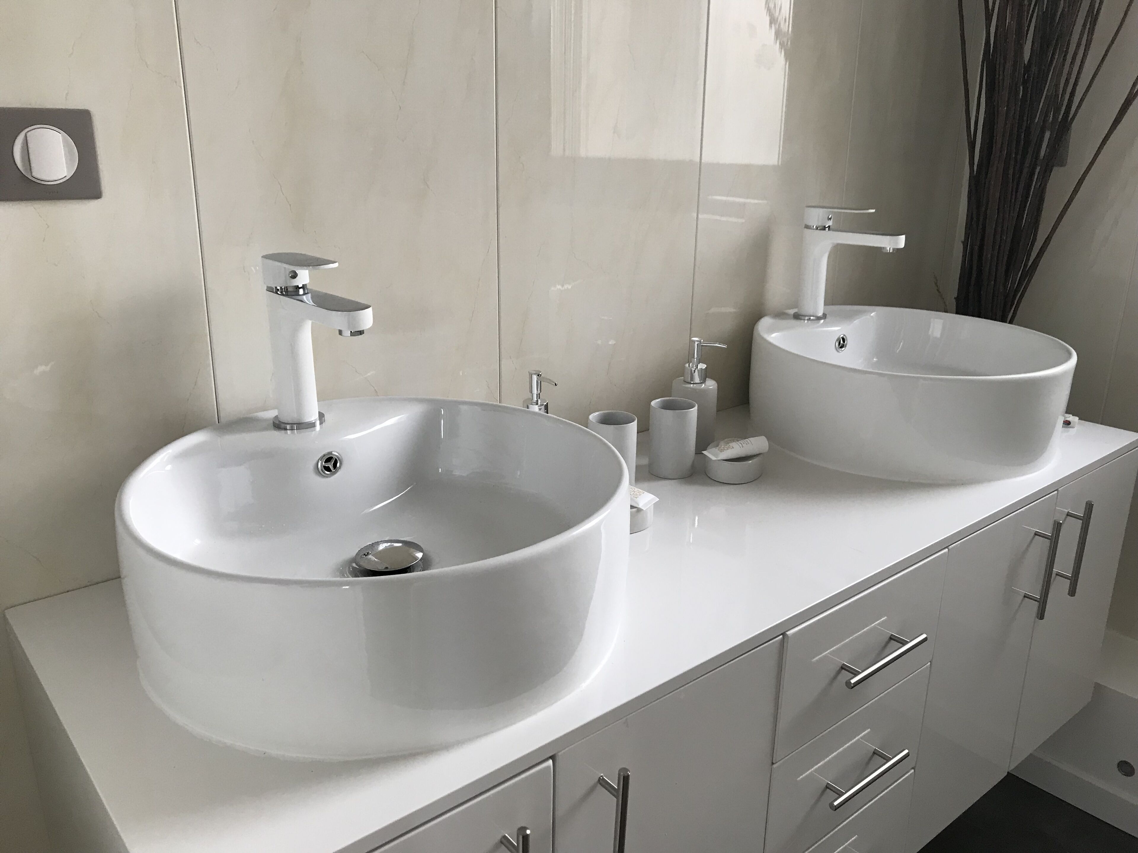 A modern bathroom with two large white sinks, a mirror, and a cabinet with drawers.