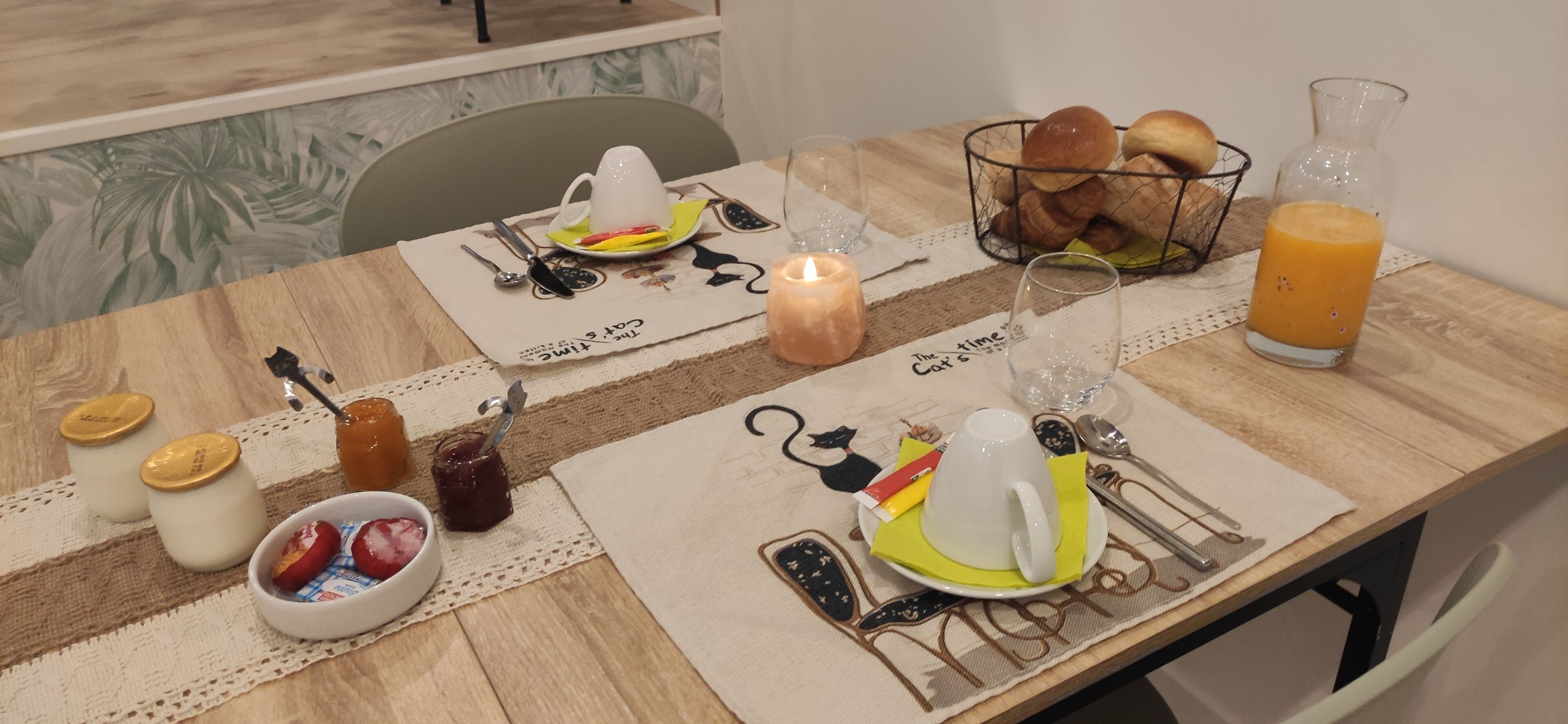 A breakfast table set with a candle, a glass of orange juice, bread, and a bowl of fruit.