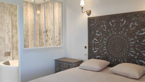 Un dormitorio con una cama grande, cabecera de madera con intrincados adornos, mesita de noche, cómoda y baño con tocador de madera y espejo.