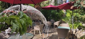 Un patio al aire libre con mobiliario de mimbre, sombrillas rojas y una estructura blanca decorativa.