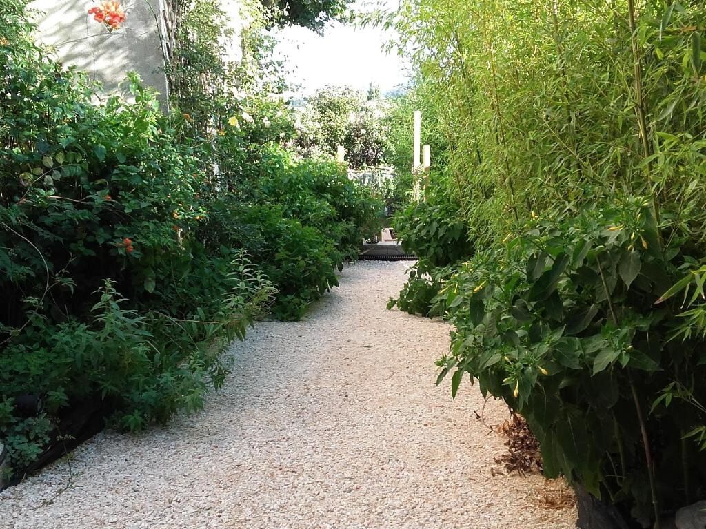 Un sentier de gravier bordé d’une végétation luxuriante et verdoyante mène à un bâtiment traditionnel doté d’un toit en tuiles.