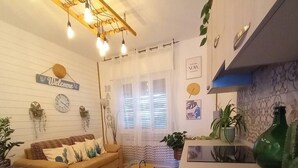 Una sala de estar acogedora con un sofá, una mesita redonda y una mesa de centro. Hay una zona de cocina con una encimera y una botella verde.
