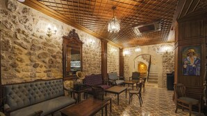 Une pièce aux murs de pierre, avec un plafond en bois et un lustre. On y trouve un canapé, une table et des chaises.