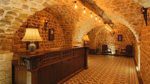 Une pièce aux murs de pierre, avec un comptoir en bois, deux lampes, une horloge et un sol à motifs.