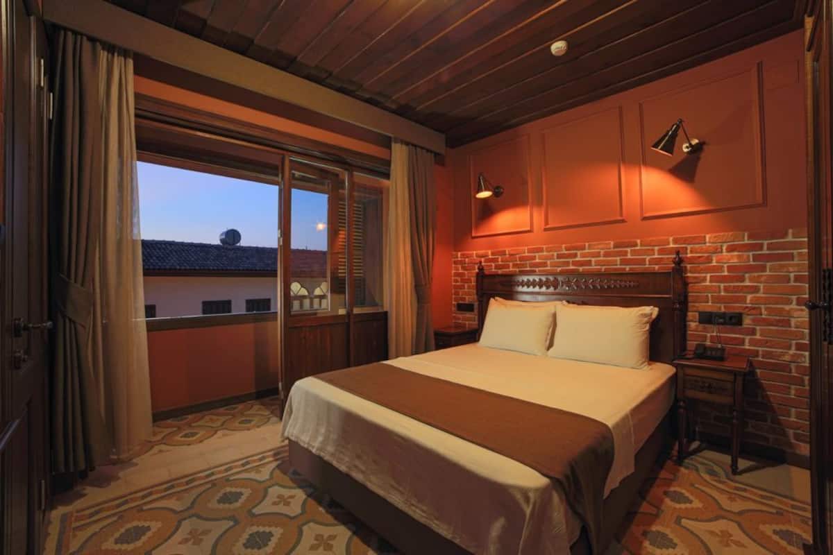 A hotel room with a large bed, a brick wall, and a view through a sliding door.