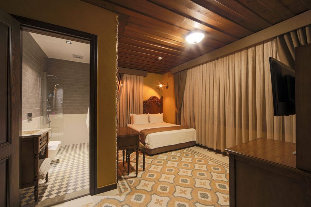 A hotel room with a bed, a desk, a television, and a bathroom visible through an open door.